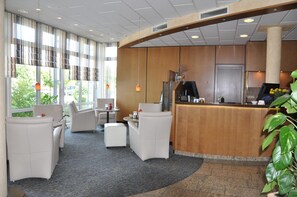 A hotel lobby with a reception desk, seating area, and large windows. - Hotel Merkur (Ramstein-Miesenbach)
