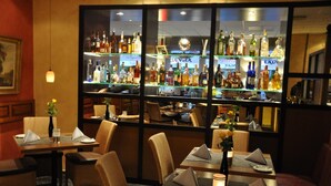 Un restaurante con zona de bar visible a través de un panel de vidrio, mostrando diversas botellas y un espejo decorativo.
