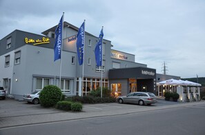 A hotel building with multiple flags, a sign reading 'hotel merkur', and a parking area with cars.