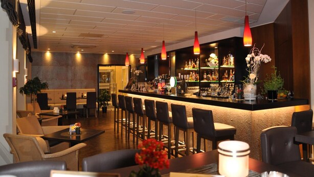 Una zona de bar con una barra larga, varios taburetes y una gran variedad de botellas y vasos.