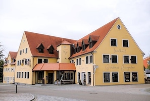 En gul byggnad med ett rött tak, märkt med skyltarna ”Wirtschaftsgebäude” och ”Lindahotel”.