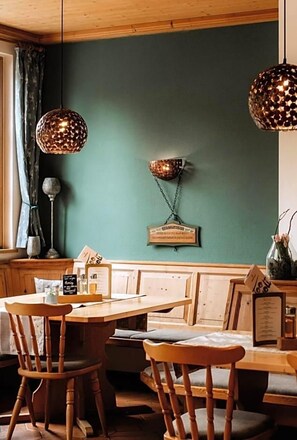 A wooden dining area with a bench and chairs, a table with a menu, and pendant lights. - Landhotel Gary (Wolframs-Eschenbach)