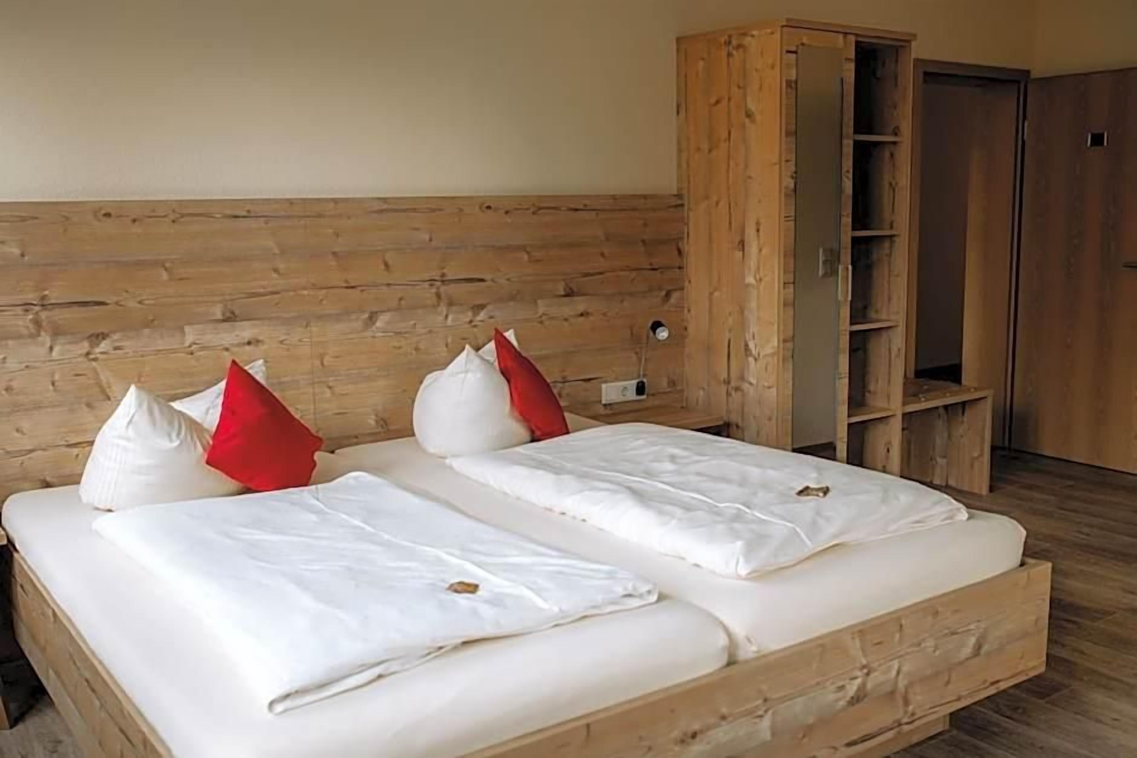 Un lit double avec une literie blanche et des oreillers rouges et blancs, une tête de lit en bois et une armoire en bois dont les portes sont ouvertes.