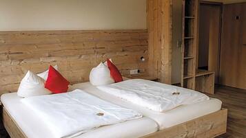 Un lit double avec une literie blanche et des oreillers rouges et blancs, une tête de lit en bois et une armoire en bois dont les portes sont ouvertes.
