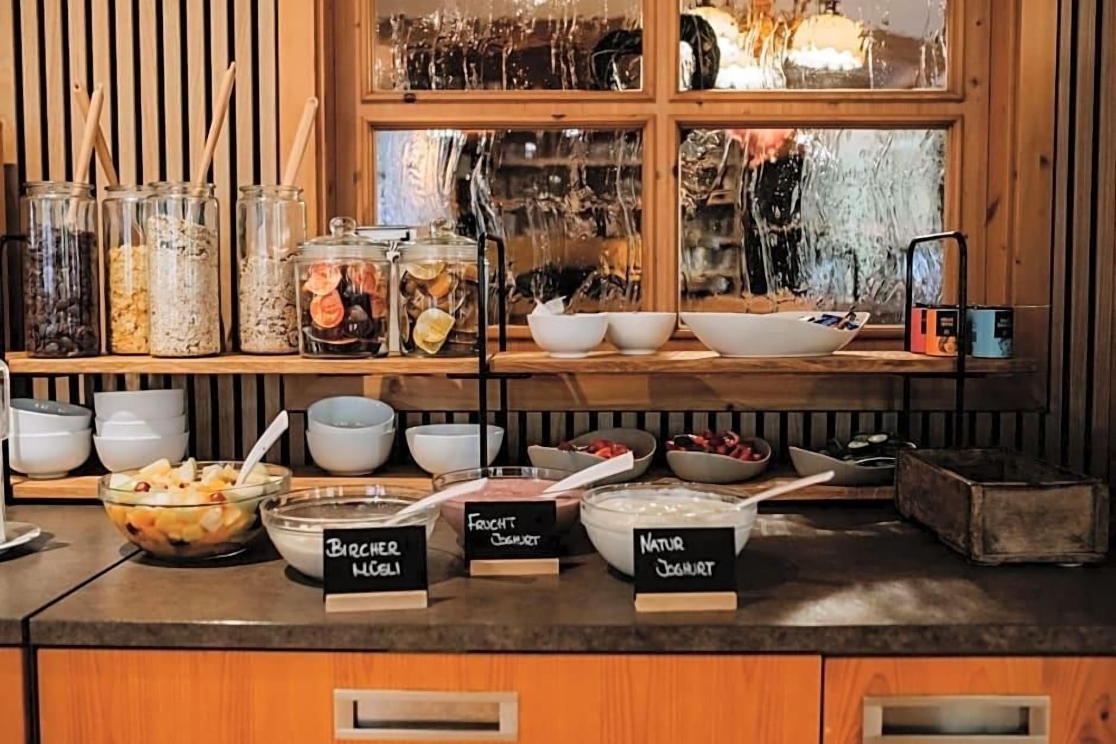 Ein Frühstücksbuffet mit beschrifteten Behältern für Müsli, Joghurt und Obst.
