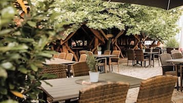 An outdoor seating area with wicker furniture and a canopy of green foliage.
