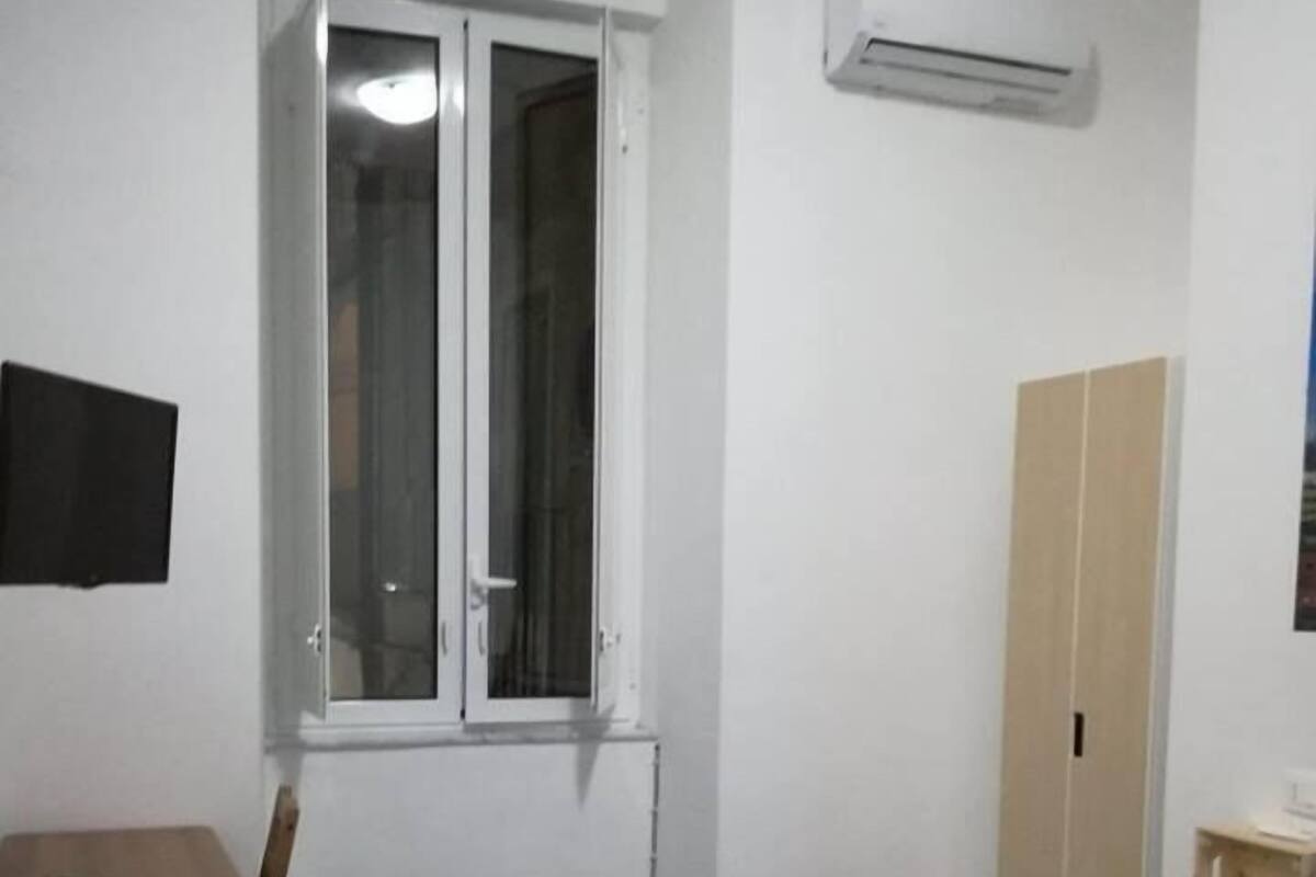 A room with a bed, a desk, a wardrobe, a window, and an air conditioning unit.