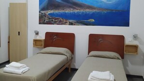 A hotel room with two beds, a painting of a coastal scene, a wardrobe, and a bedside table with a lamp. - Domus 19 (Naples)
