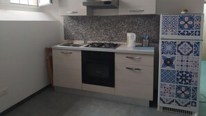 A compact kitchen with a gas stove, sink, and a microwave. There are cabinets above the counter and a window on the left. - Domus 19 (Naples)