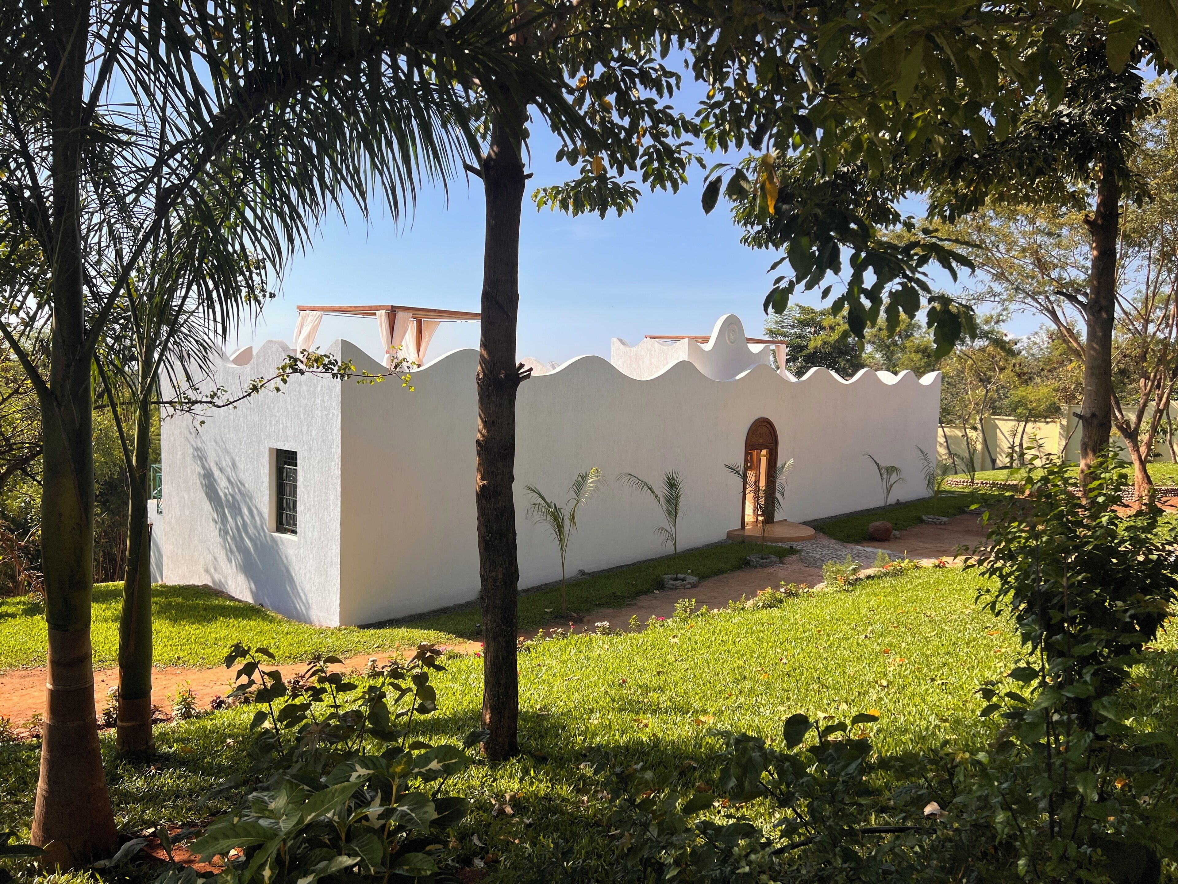 A small, white building with a single arched entrance, surrounded by lush greenery and trees.