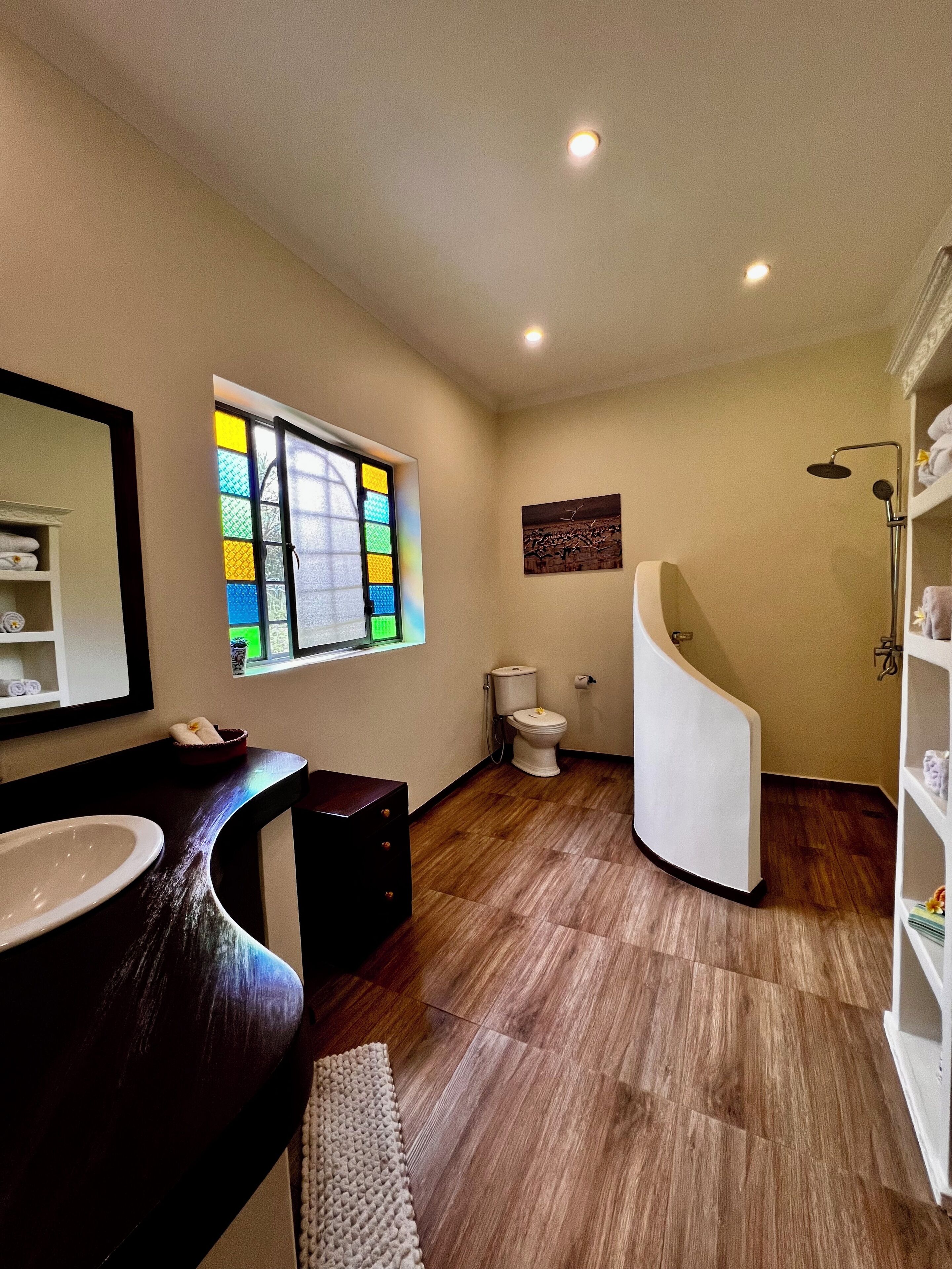 Une salle de bain moderne avec un meuble-lavabo aux lignes courbes, des toilettes, une douche et un vitrail.