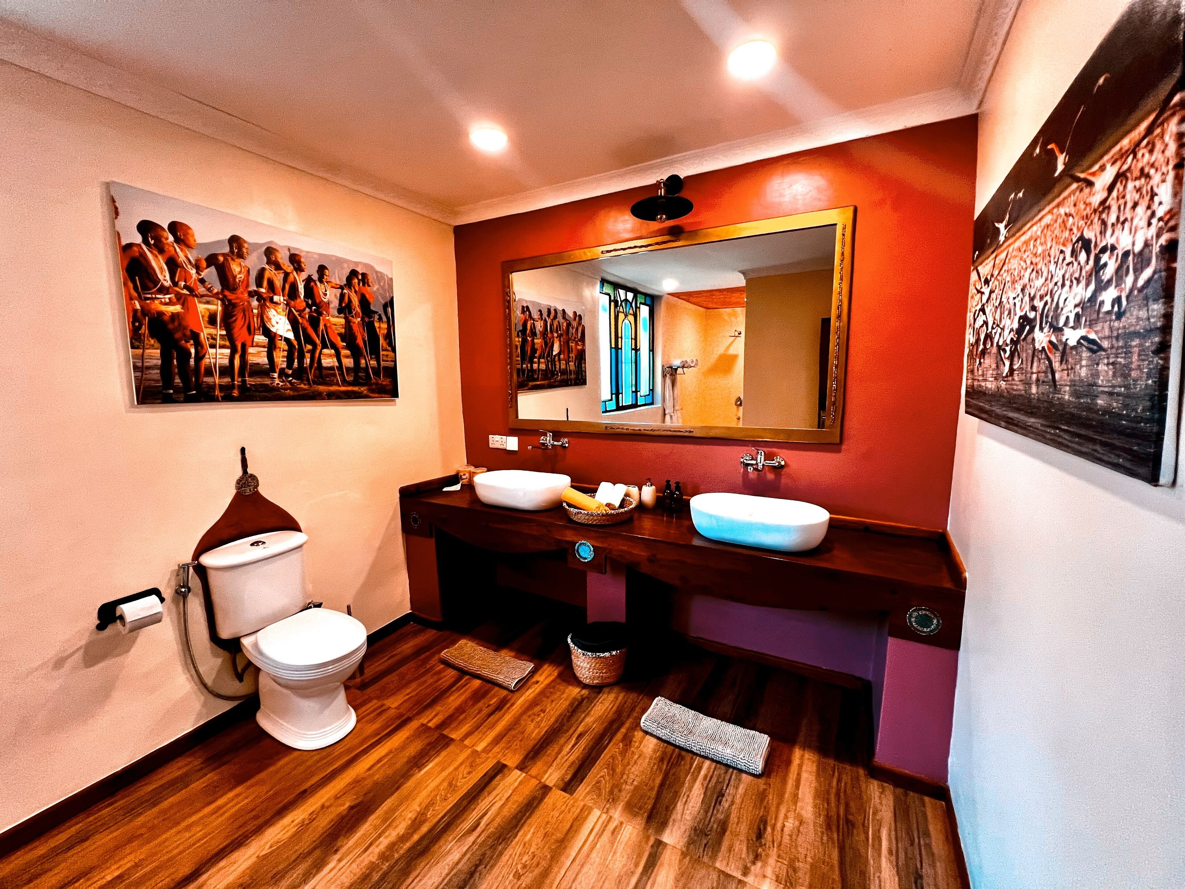 A bathroom with a wooden floor, a white toilet, a double sink vanity, and a large mirror.