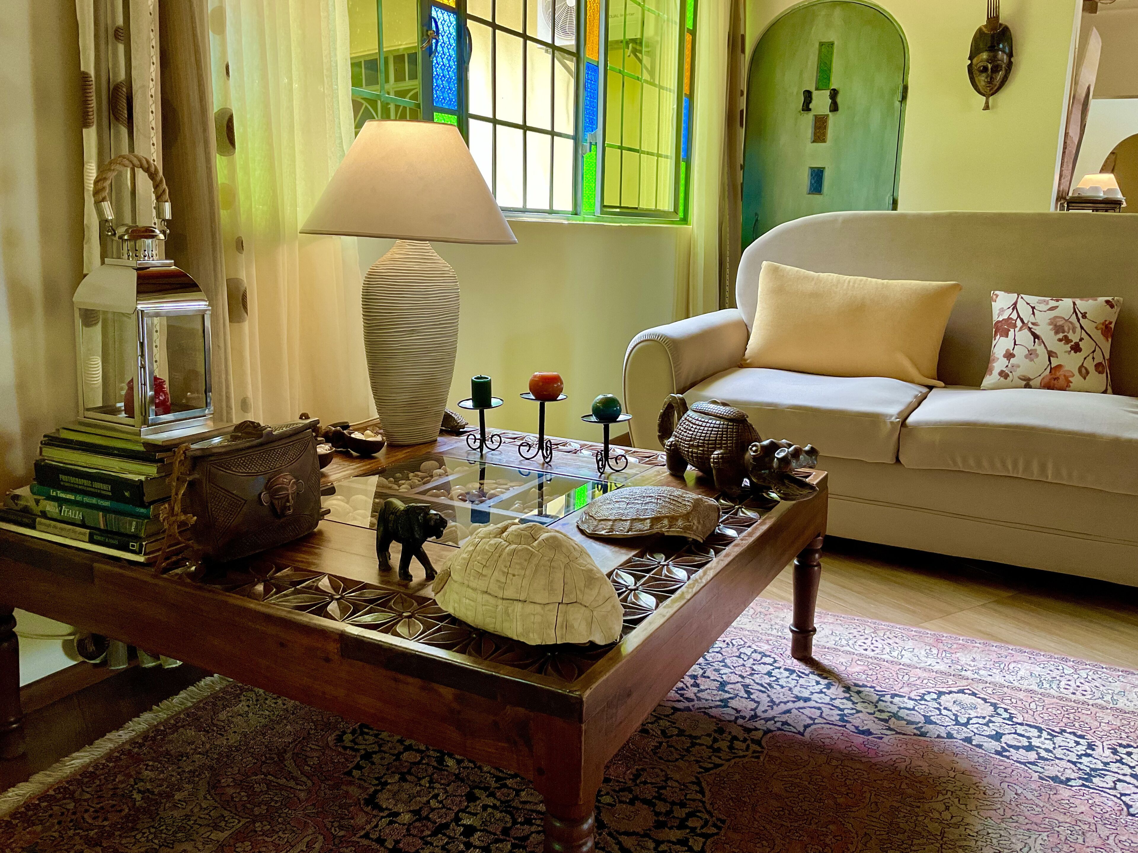 A living room with a coffee table, books, decorative items, a sofa, and a window with green-tinted glass.