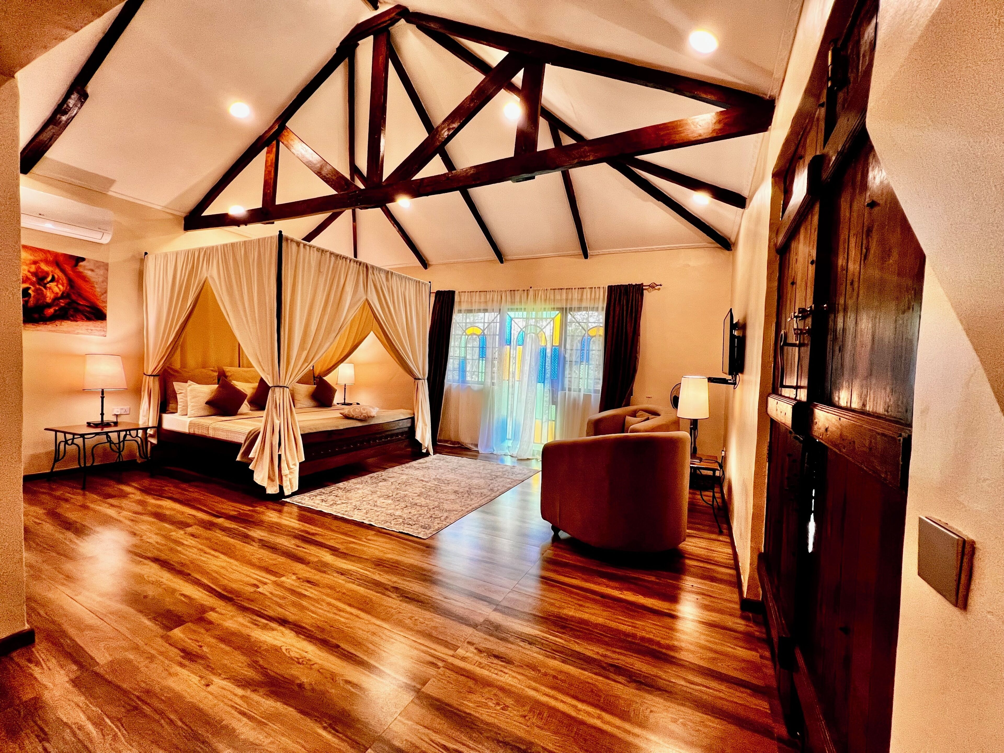 Ein Schlafzimmer mit Himmelbett, einer Sitzecke mit einem Sessel, Holzboden und einer geneigten Decke mit freiliegenden Balken.