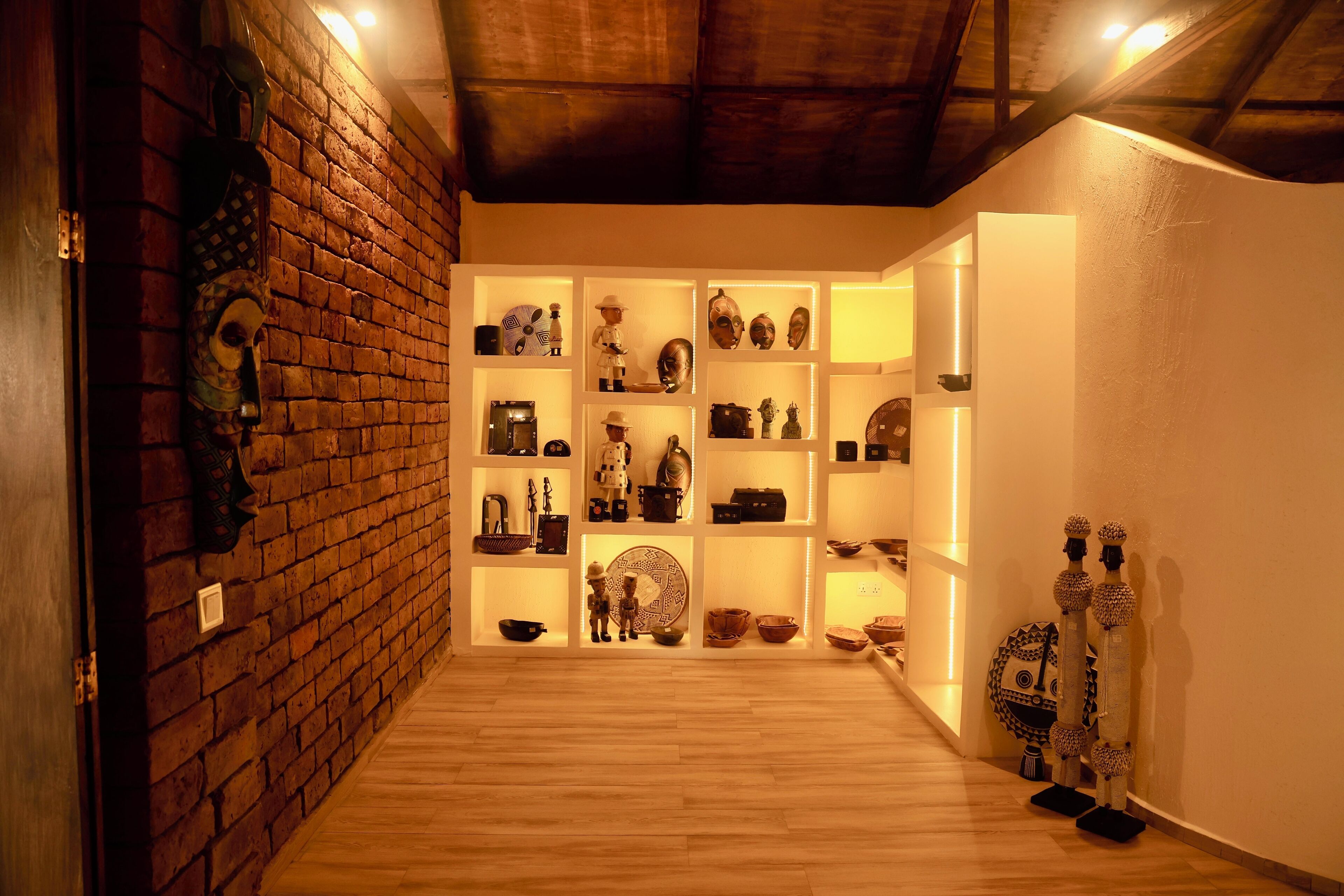 A hallway with brick walls and wooden flooring, leading to a room with shelves displaying various artifacts.