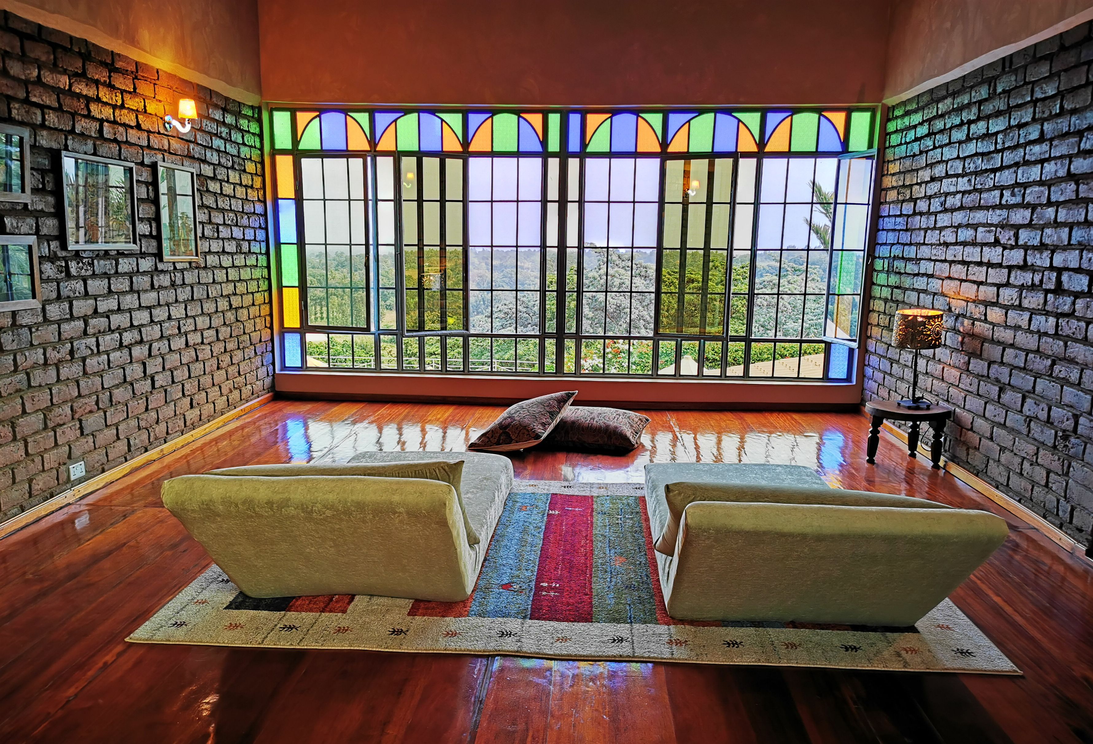 Une pièce avec un mur en briques, une grande fenêtre ornée de vitraux colorés, deux fauteuils et une petite table.