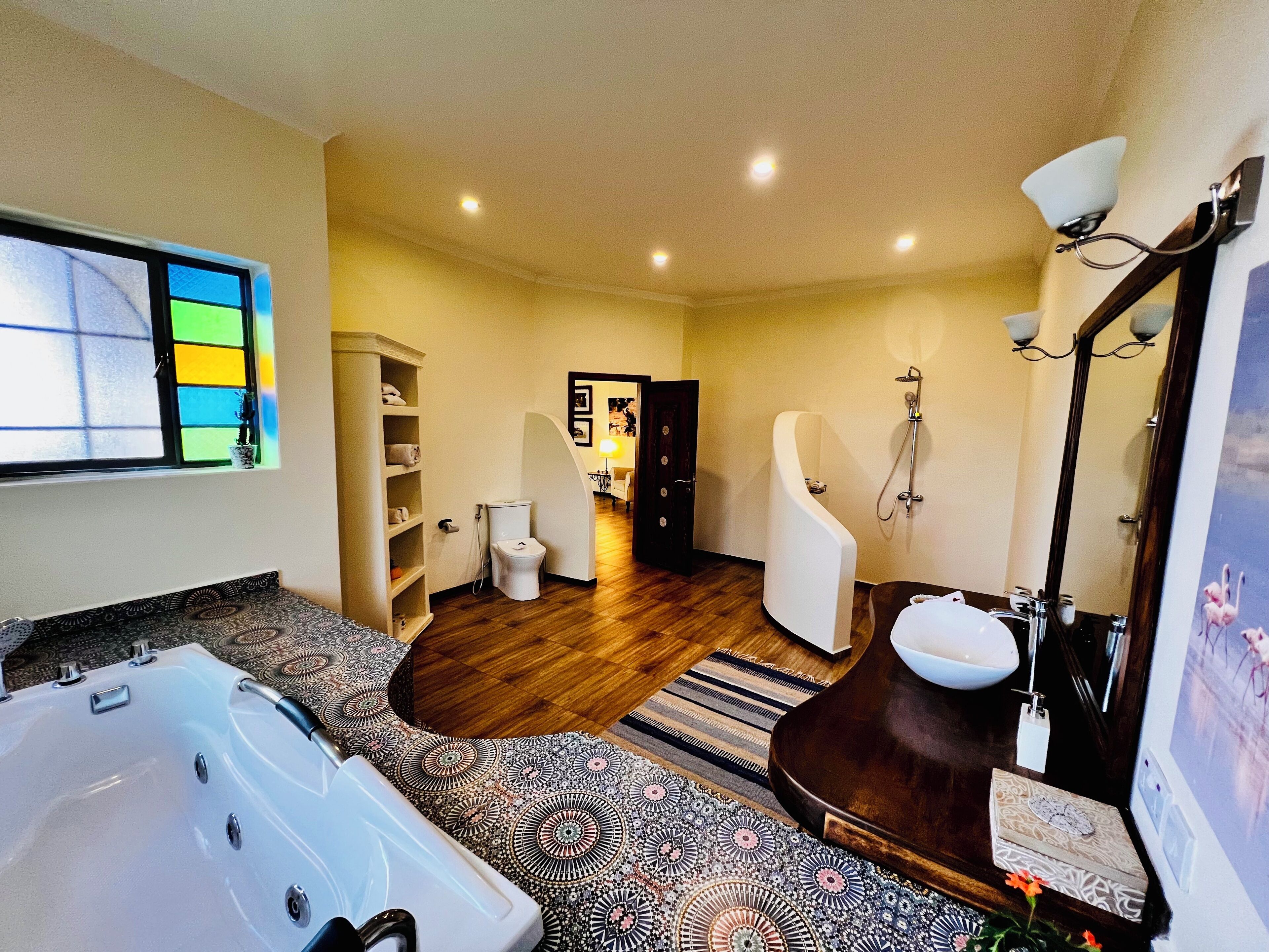 Un baño moderno con bañera, ducha y retrete. El suelo es de madera y hay una alfombra estampada.