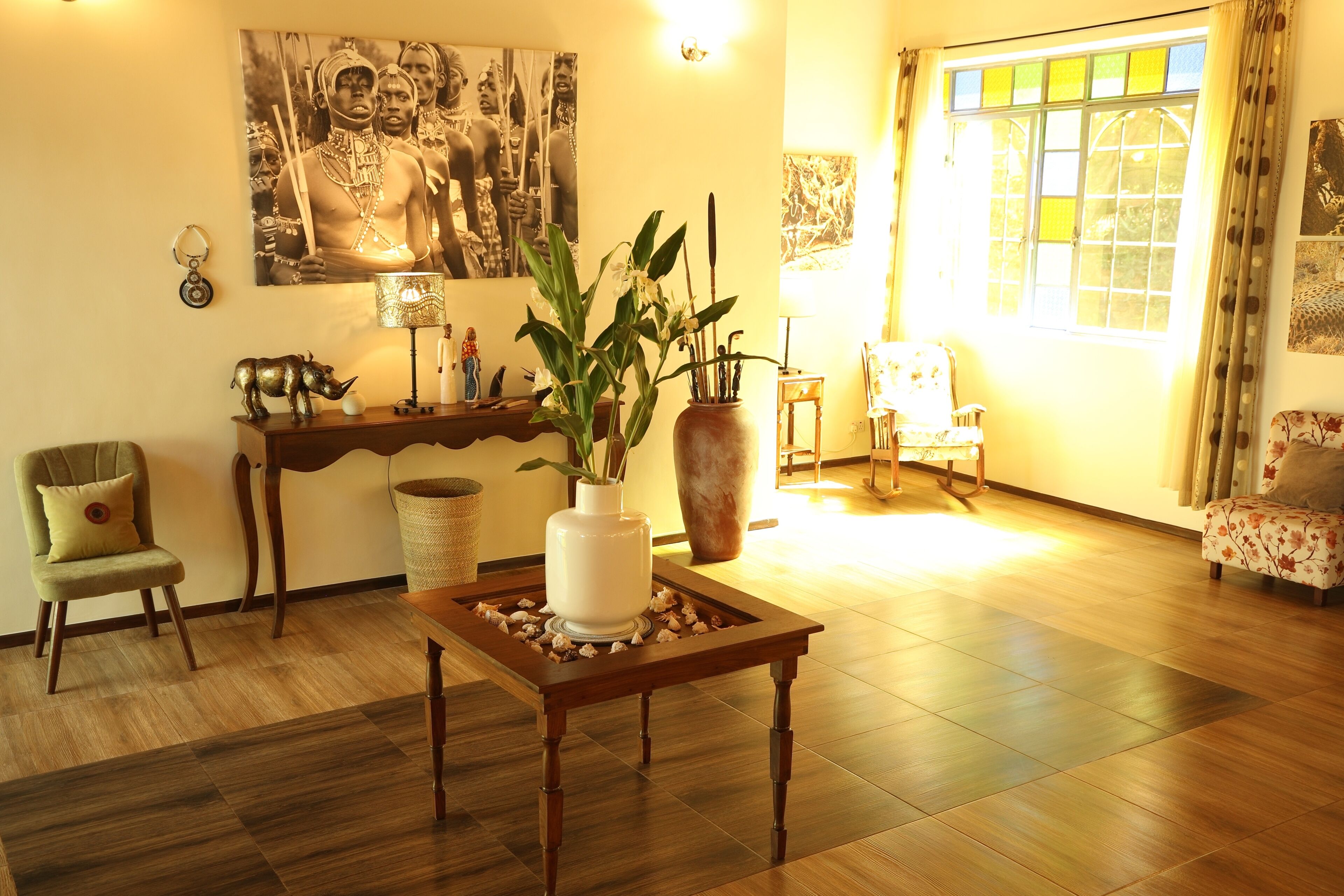Una sala de estar con una mesa de centro de madera, una planta en maceta, un sofá, una silla y un ventanal con cortinas.