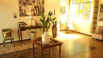 Una sala de estar con una mesa de centro de madera, una planta en maceta, un sofá, una silla y un ventanal con cortinas.