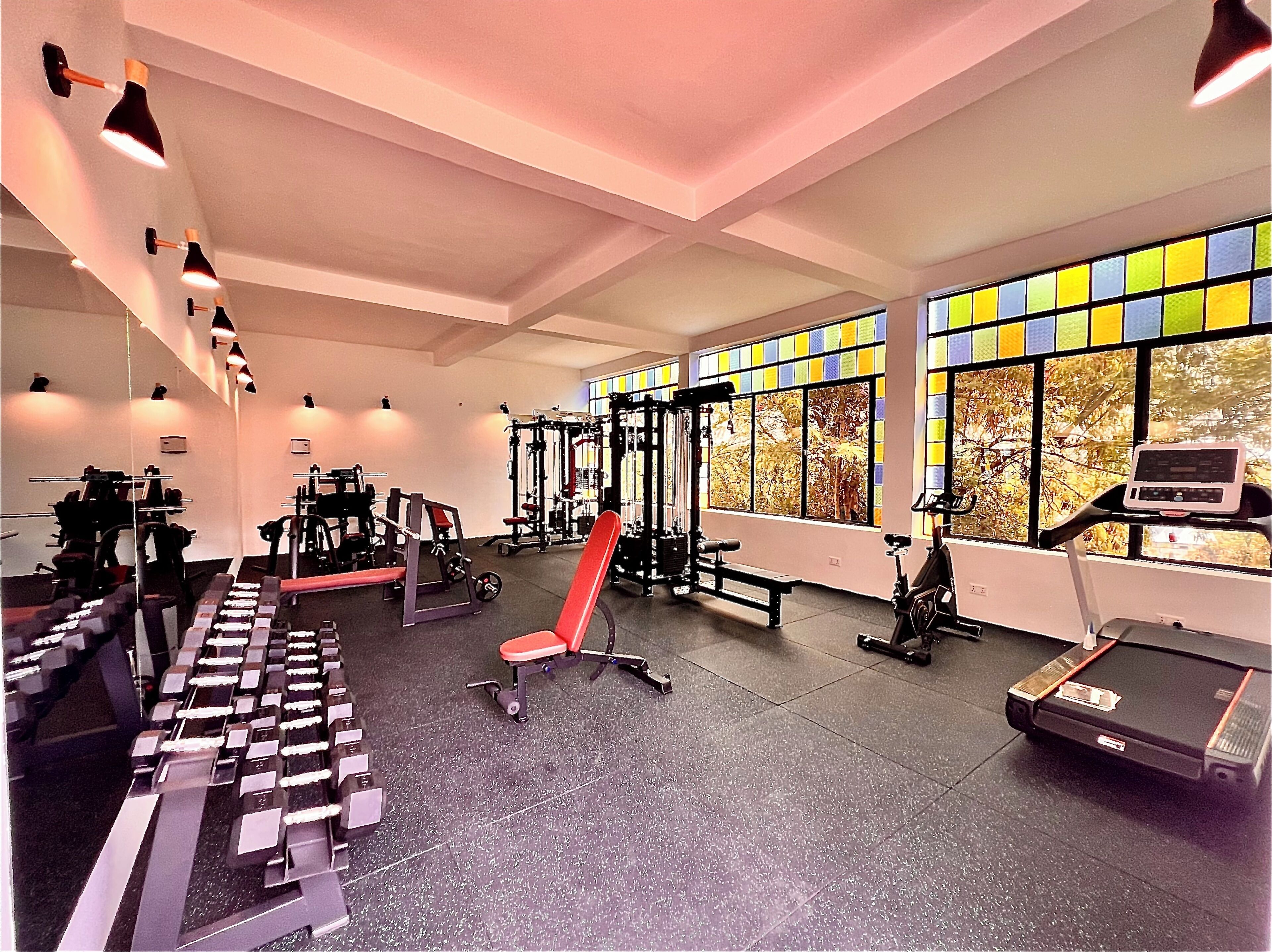 A gym with exercise equipment, a bench, and large windows with a view of trees.