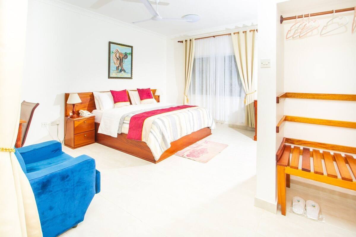 A bedroom with a bed, bedside table, lamp, and a blue chair.