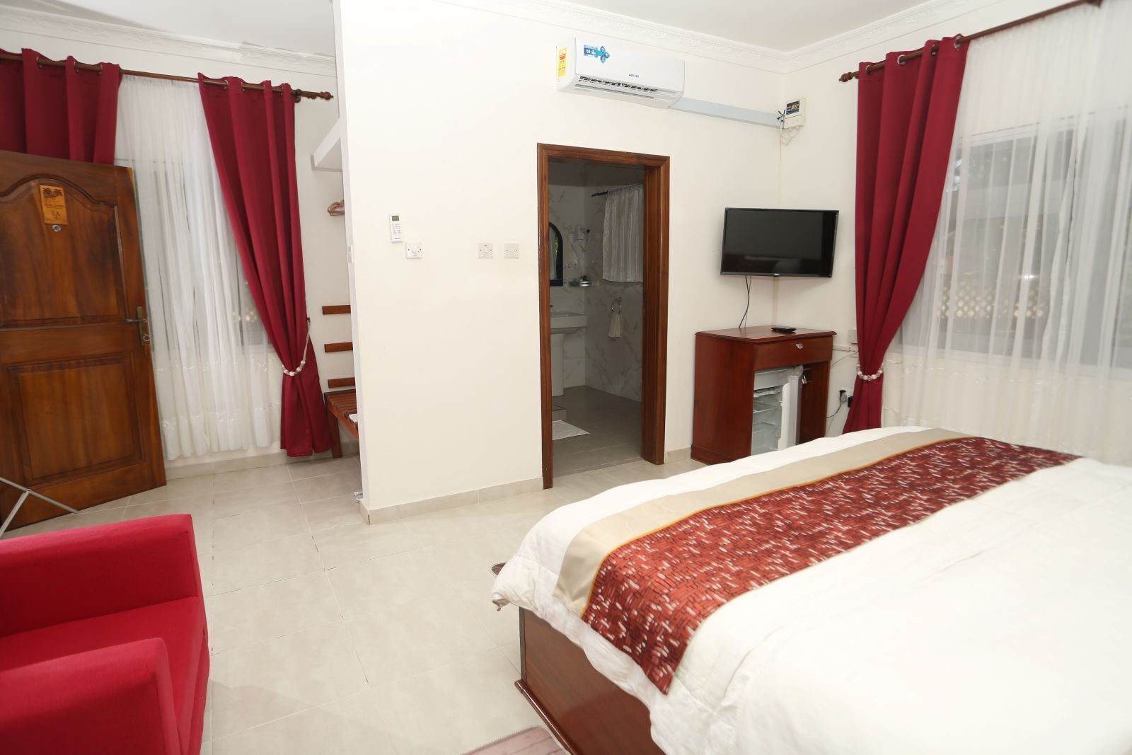 A hotel room with a bed, a TV, a wardrobe, and a bathroom visible through an open door.