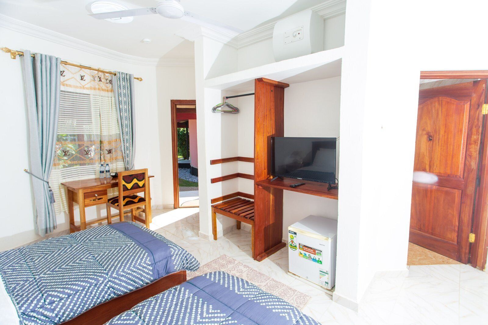 Un dormitorio con una cama, un escritorio, un televisor y un refrigerador pequeño.