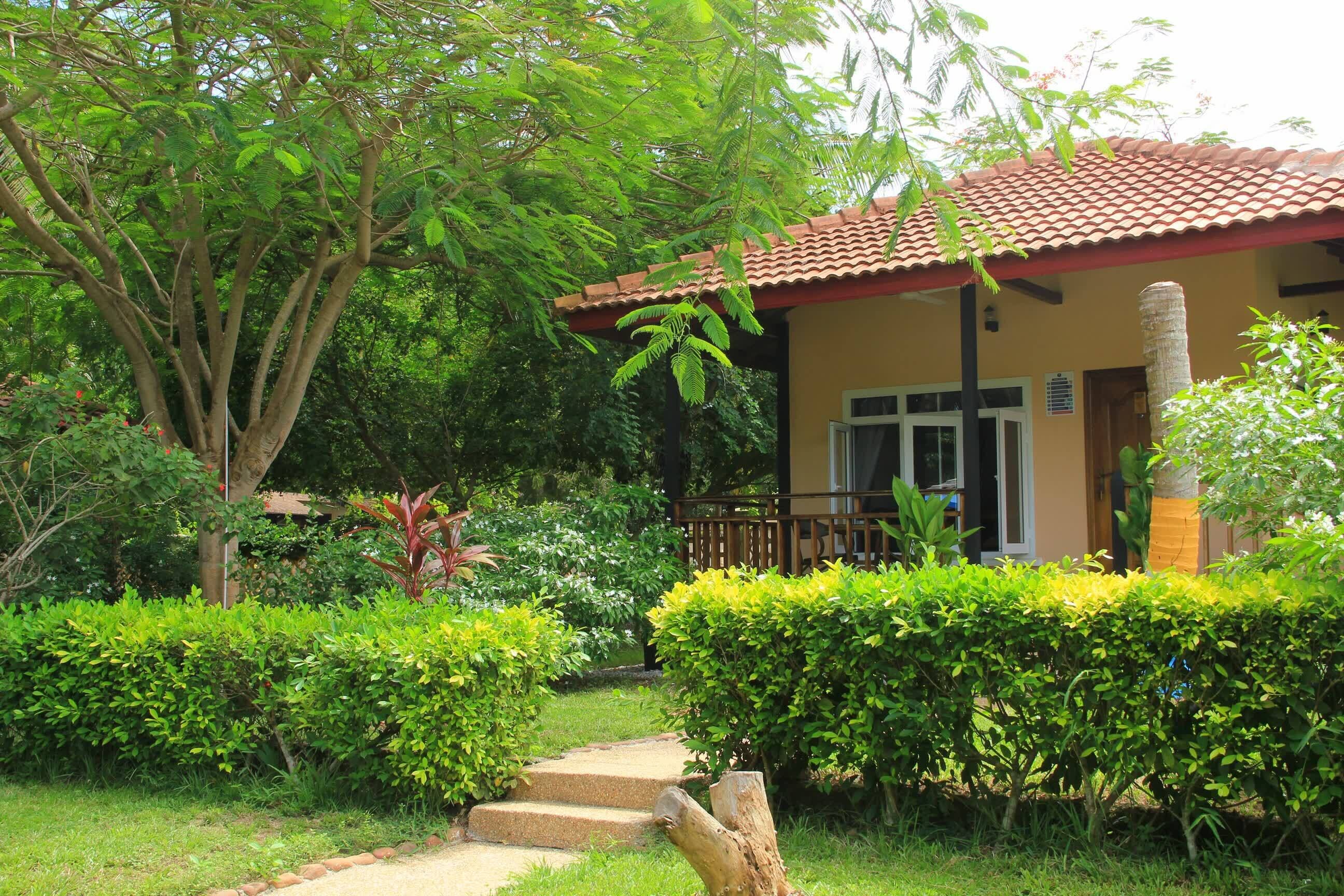 A house with a red-tiled roof, surrounded by lush greenery and a well-maintained garden.