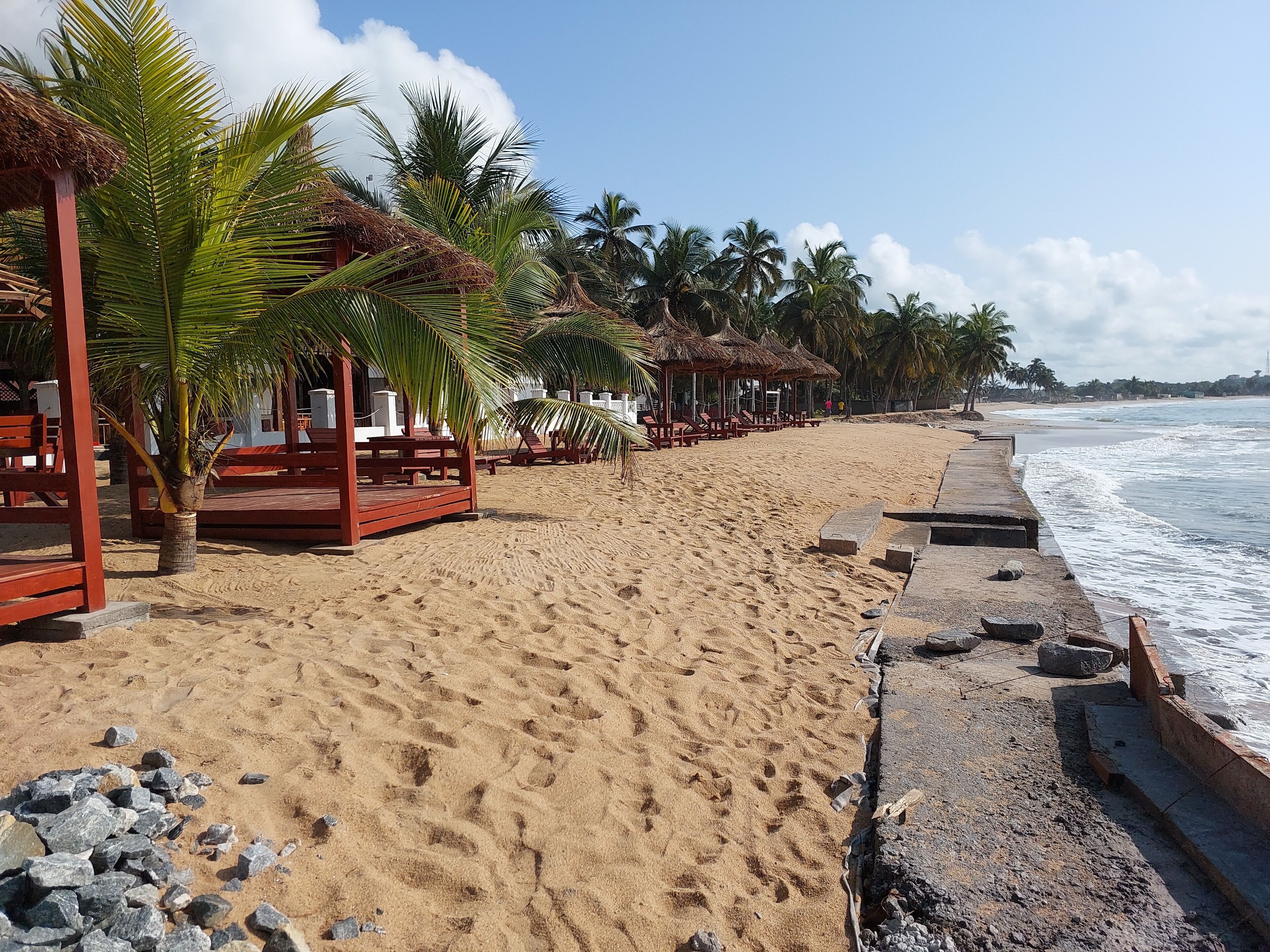 A beach with thatched-roof structures and palm trees.