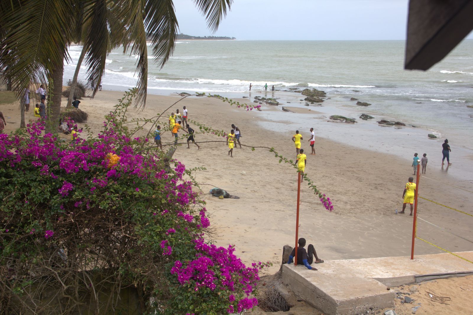 Una playa con gente jugando, una estructura de concreto y flores moradas.