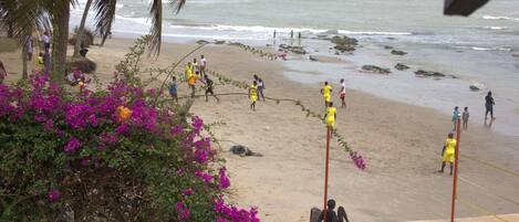 Una playa con gente jugando, una estructura de concreto y flores moradas.