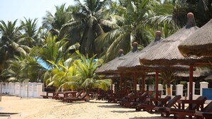 A beach with thatched umbrellas and wooden lounge chairs, surrounded by palm trees. - Charlestina Beach Resort (Ampenyi)