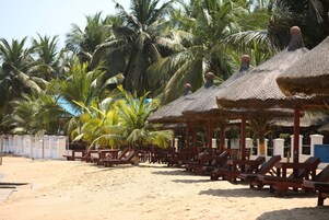 A beach with thatched umbrellas and wooden lounge chairs, surrounded by palm trees.