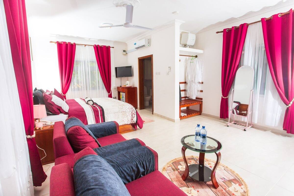 A hotel room with a bed, a sofa, a TV, a mirror, and a small table with water bottles.