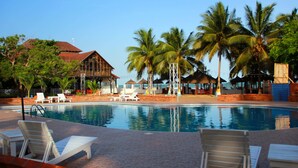 A pool area with lounge chairs, palm trees, and a building with a red roof. - Charlestina Beach Resort (Ampenyi)