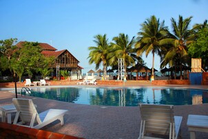 A pool area with lounge chairs, palm trees, and a building with a red roof.