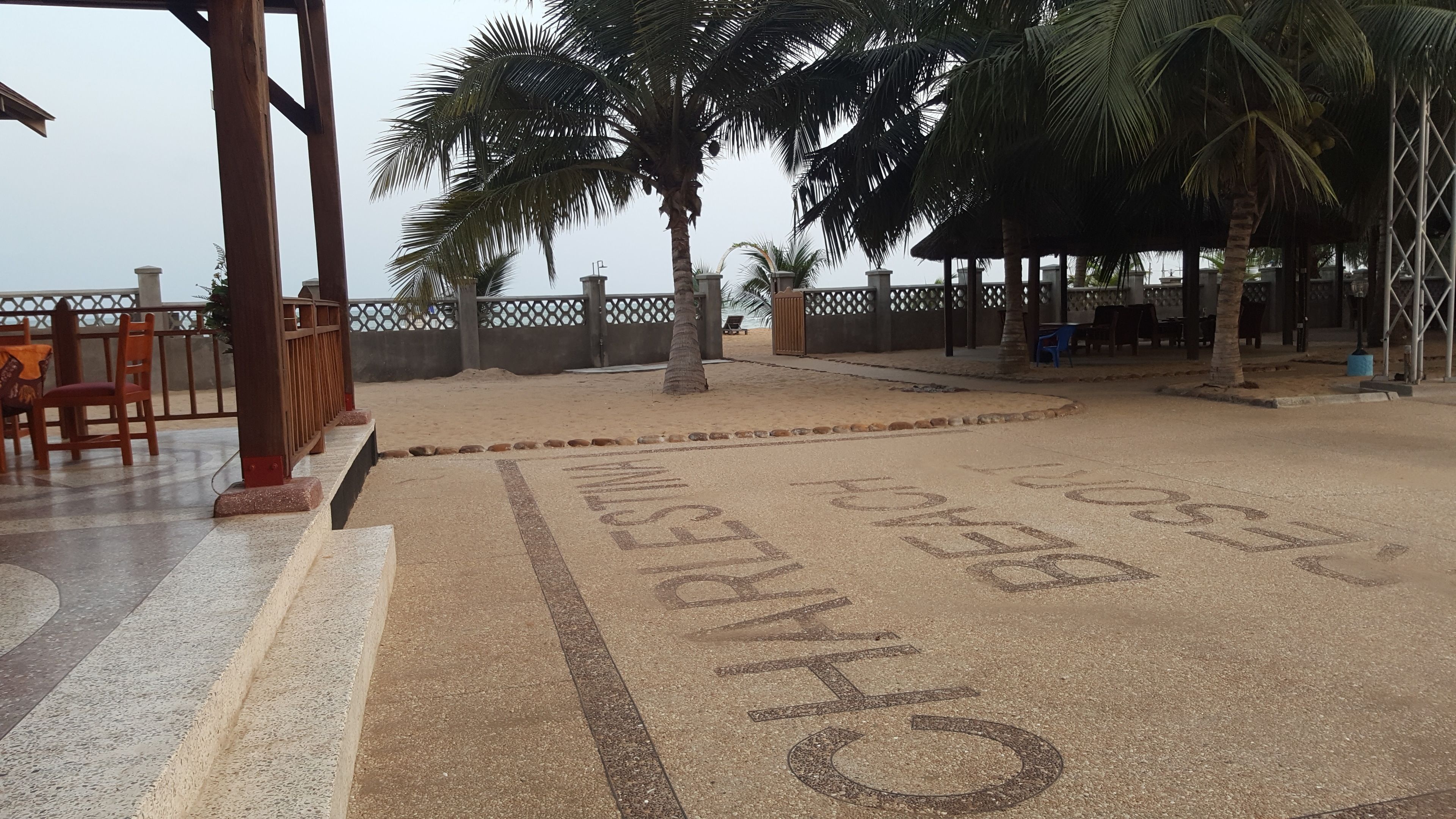 Una spiaggia con palme, un pergolato in legno e un'area relax con sedie.