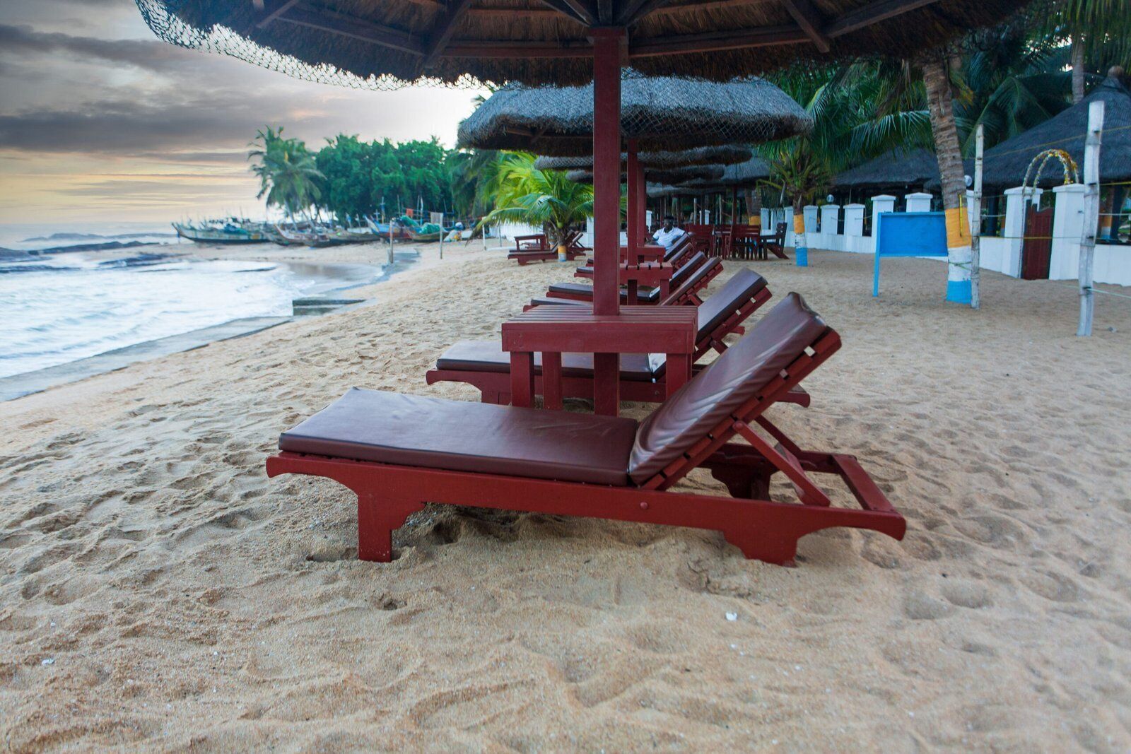 Une plage avec des chaises longues rouges et des parasols en chaume.