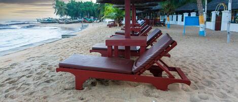 Une plage avec des chaises longues rouges et des parasols en chaume.