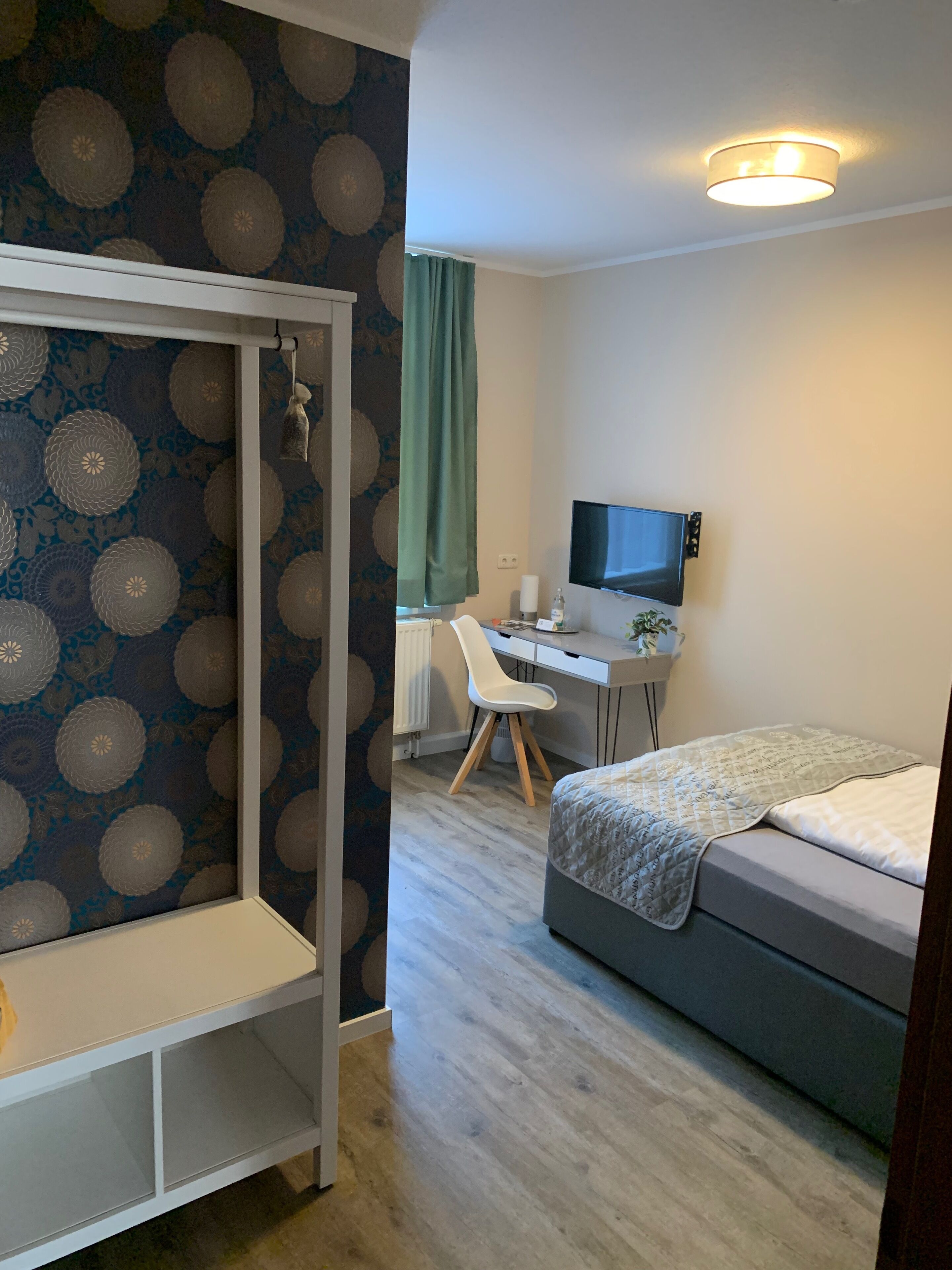 Een slaapkamer met een bed, bureau met stoel, televisie en een kledingkast.