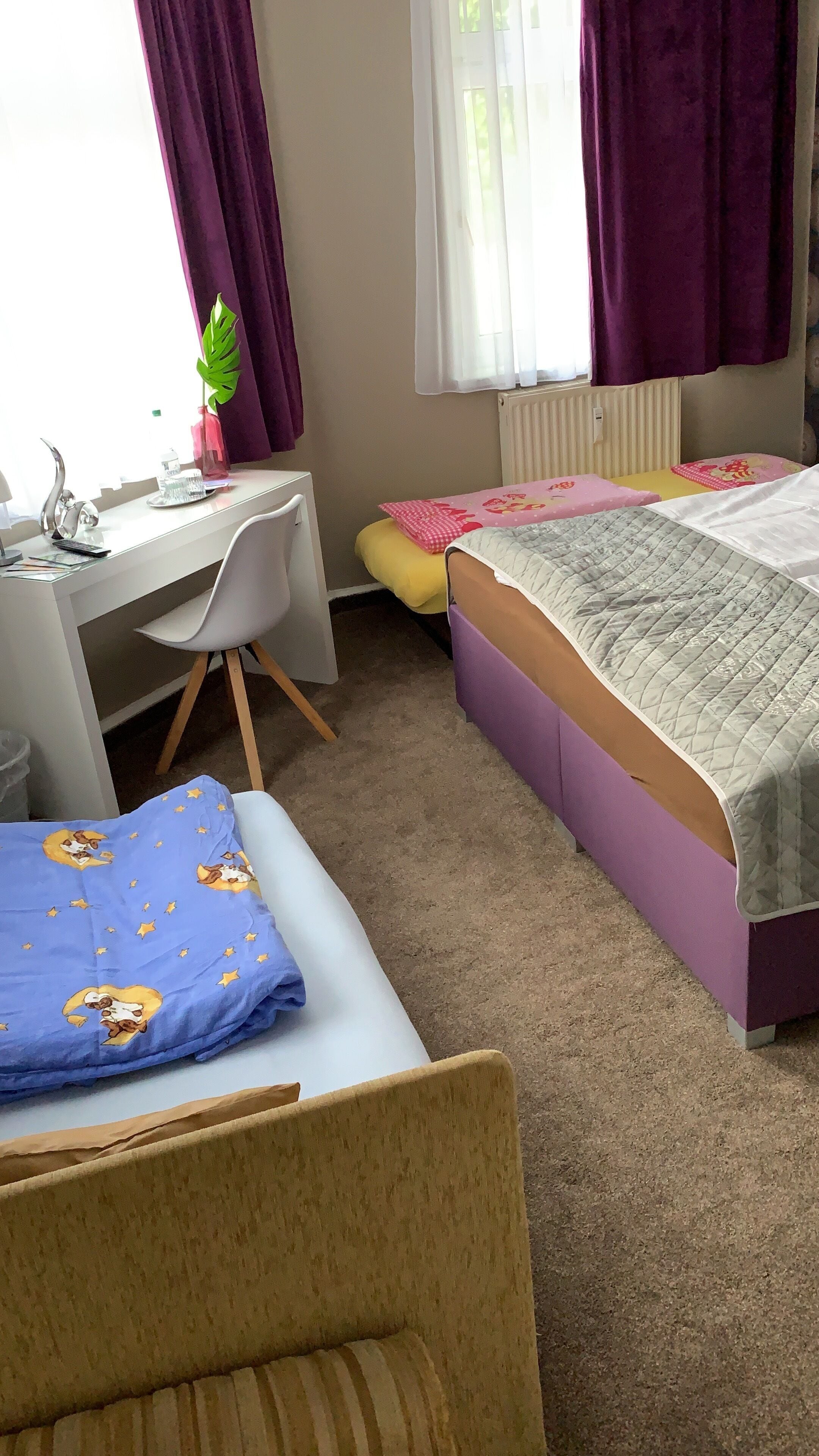 Ein Schlafzimmer mit Schreibtisch, zwei Betten, einem Sessel und einer Heizung.
