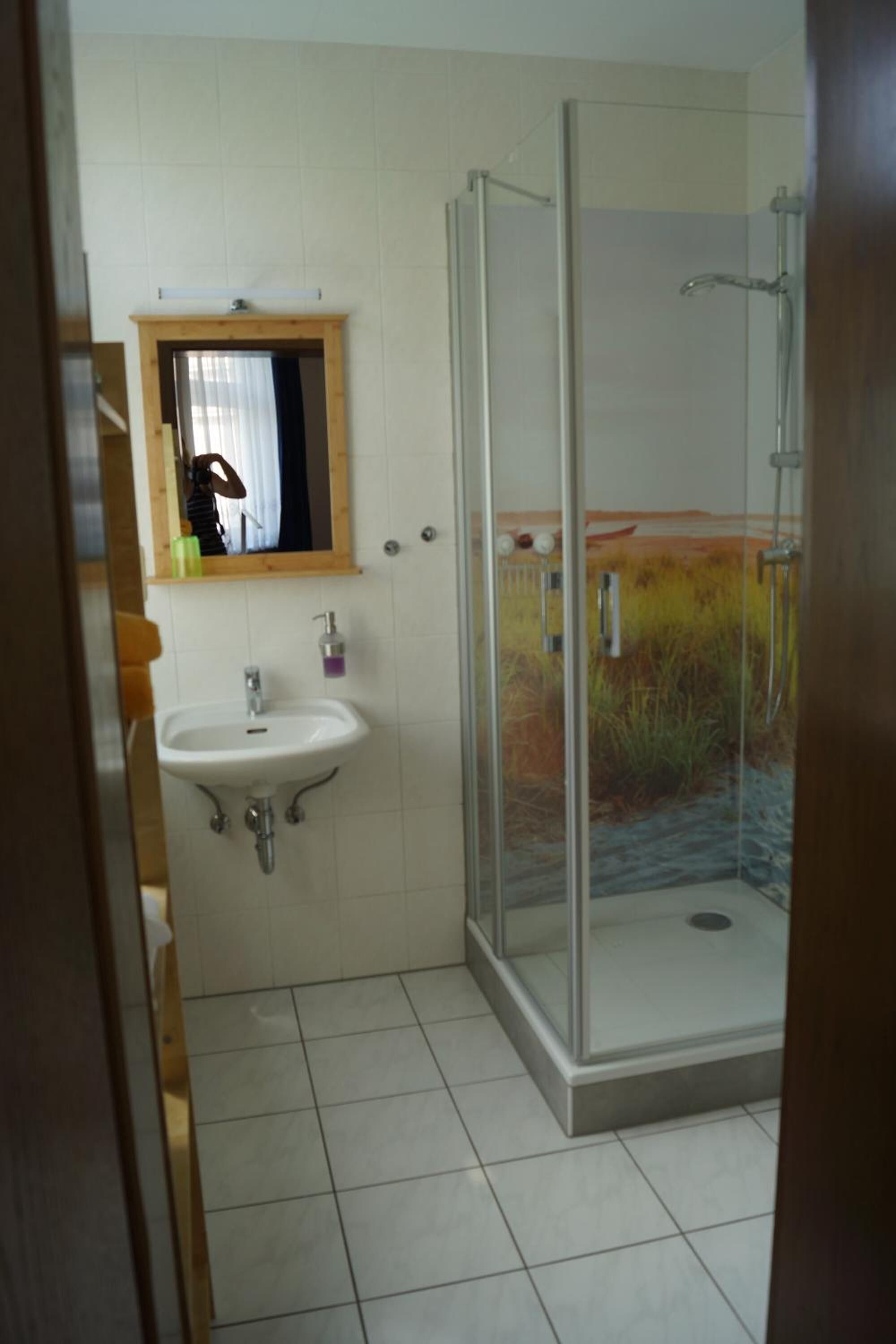 Een badkamer met een douchecabine van glas, een wastafel met spiegel erboven en een betegelde vloer.