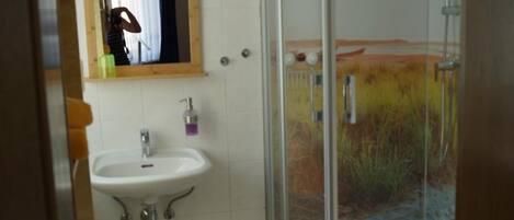A bathroom with a glass shower enclosure, a sink with a mirror above it, and a tiled floor.