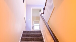A staircase with carpeted steps and a wooden handrail, leading to a doorway.