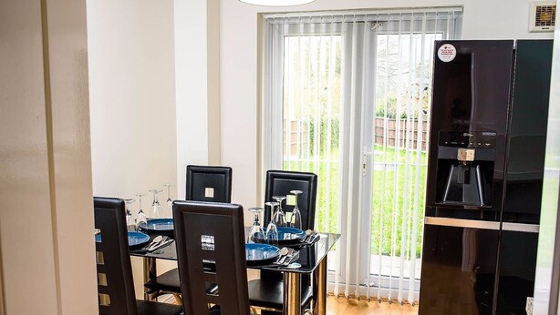 A dining area with a table set for four, chairs, a water dispenser, and a view of a garden through a glass door.