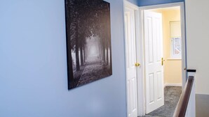 A hallway with a framed black and white photograph on the wall, white doors, and a carpeted floor.