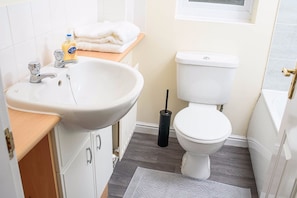 A bathroom with a white sink, a toilet, a window, and a towel stack. - Crystal (Manchester)