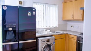 A compact kitchen with a refrigerator, washing machine, sink, and wooden cabinets.