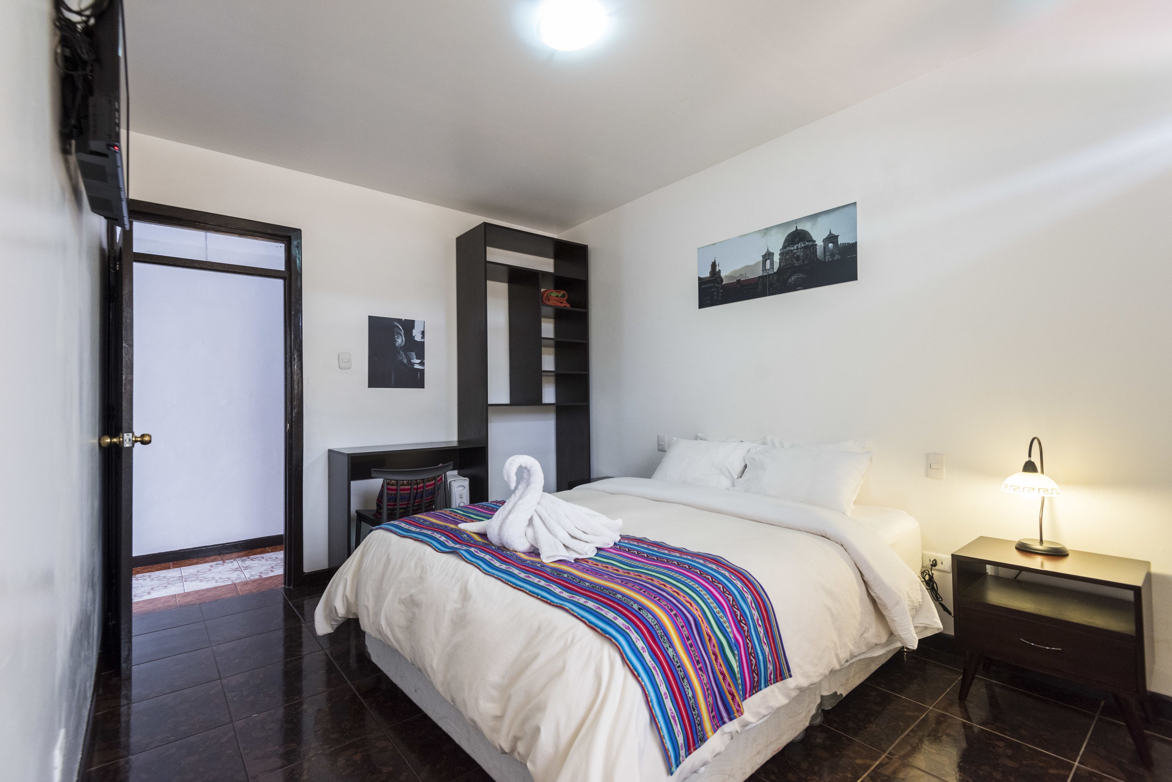 A hotel room with a bed, a desk, a chair, a nightstand, a lamp, and a painting on the wall.
