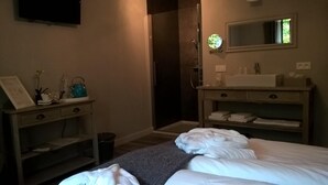 Habitación de hotel con cama, mesita de noche con lámpara, espejo, zona de ducha y un pequeño escritorio con silla.